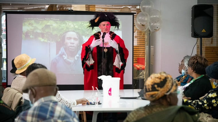 A man in red and black costume speaking in front of the audience