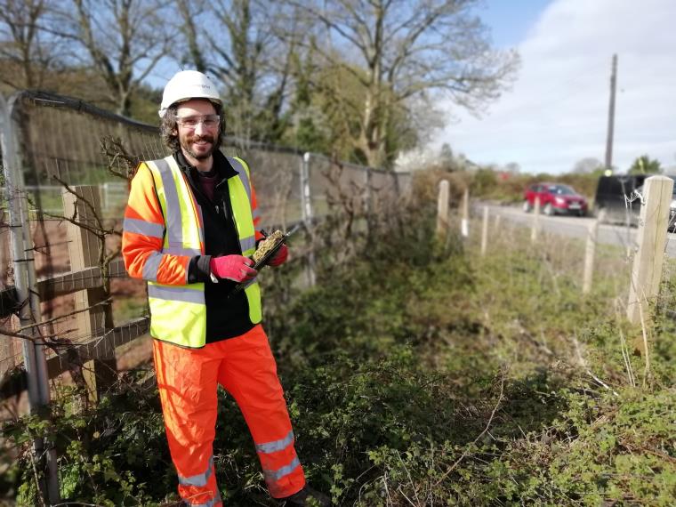 An engineer in orange uniform and reflective vest standing on the side of the road.
