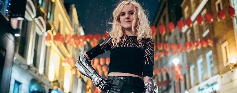 Woman wearing bionic arm smiling down to camera in a city setting.