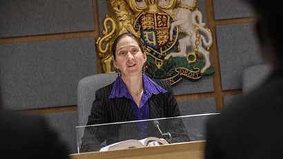 Woman in black suit and purple shirt speaking giving evidence in court.