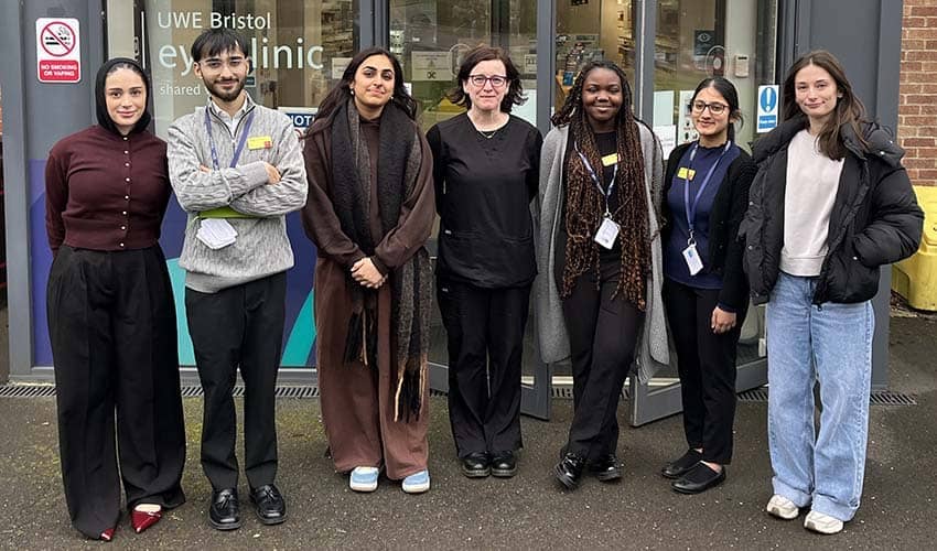 A group shot of seven students stood outside of a university building looking at the camera