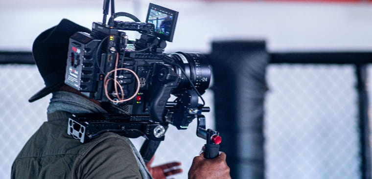 Back of a man holding a large digital camera on his shoulder.
