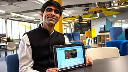 A person sat at a table holding a tablet computer, with chairs and desks in the background