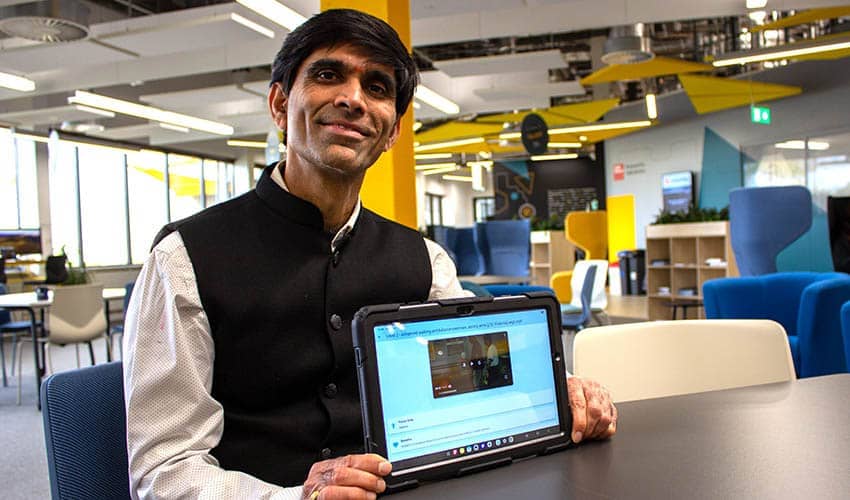 A person sat a table holding a tablet computer, with chairs and desks in the background
