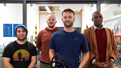 A team photo of four men stood together facing the camera in a mechatronics laboratory at a university