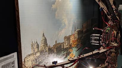 A scanner scans a piece of artwork showing a scene in Venice with boats in front of some older buildings.