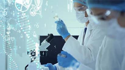 Two people in while lab clothing and face masks working with a flask, a syringe and a microscope.