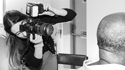 Black and white image of a woman taking a photo of the side of a man's head using a professional camera