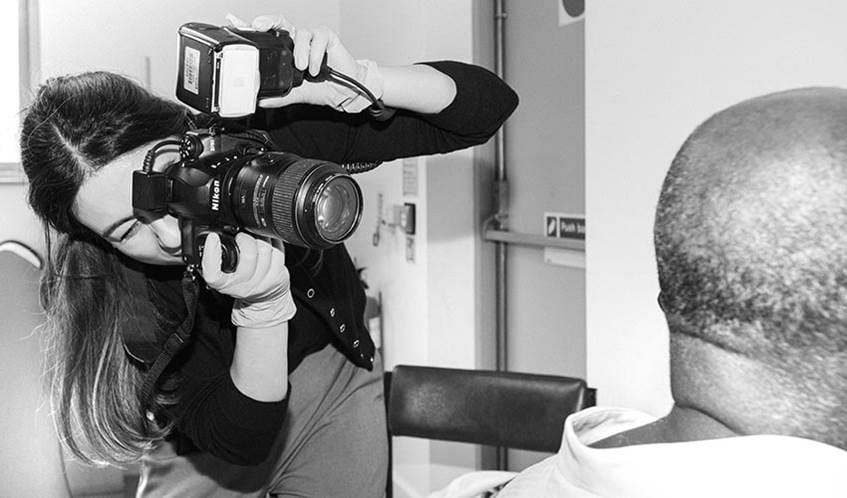 Black and white image of a woman taking a photo of the side of a man's head using a professional camera