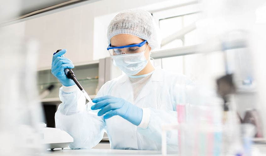 A female researcher dressed in protective clothing and safety goggles holding a pipette in a science laboratory