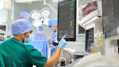 Man in green scrubs and face mask pressing large computer monitor.