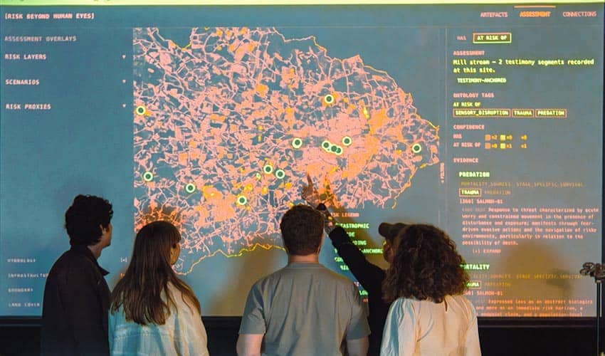 A photo looking at the backs of five people studying a digital map on a large screen