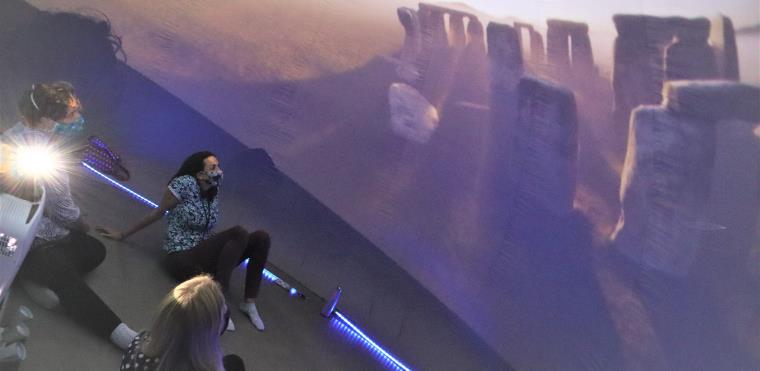 Two people sitting on floor of planetarium looking up at night sky display.