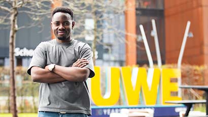 UWE Bristol international student Sadock John, photographed at Frenchay campus in front of a yellow UWE sign