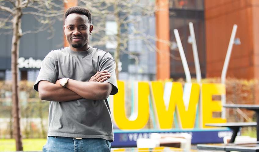 UWE Bristol international student Sadock John, photographed at Frenchay campus in front of a yellow UWE sign