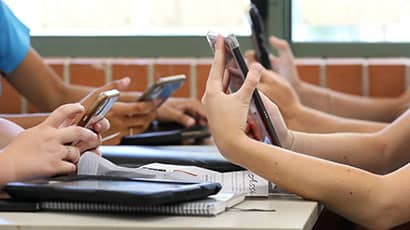 Close up image showing the hands and arms of four school pupils using their smartphones