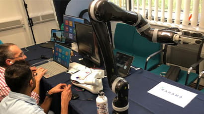 People sitting at a desk operating laptops connected to robotic arms.