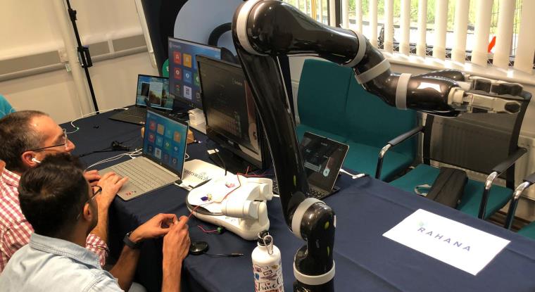 People sitting at a desk operating laptops connected to robotic arms.