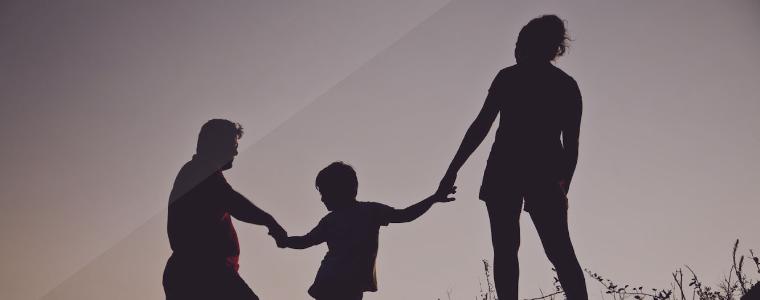 Silhouette of two adults each holding a child's hand.