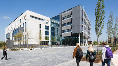 Exterior of Business School building in campus setting with four students walking towards it in foreground.