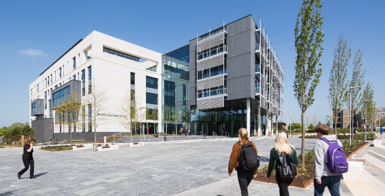 Exterior of Business School building in campus setting with four students walking towards it in foreground.