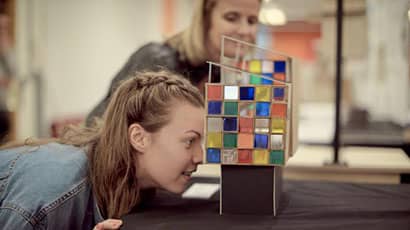 Person crouching to look through a coloured glass box art work.