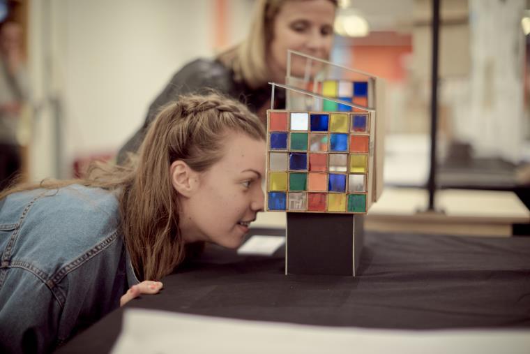 Person crouching to look through a coloured glass box art work.