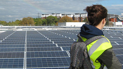 A person in a high viz jacket looks at a rooftop covered in solar panels.