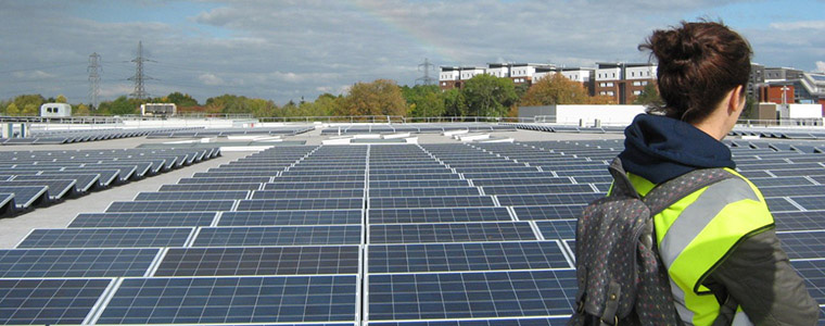 A person in a high viz jacket looks at a rooftop covered in solar panels.