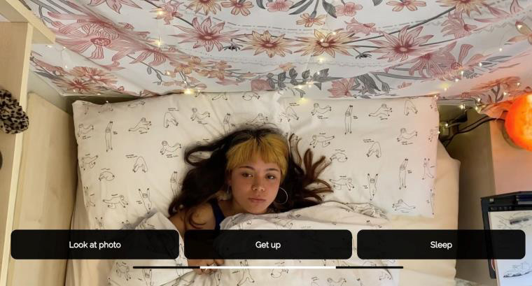 An image still from new film showing a woman lying in bed with three boxes at the bottom of the screen reading "Look at photo", "Get up", and "Sleep"