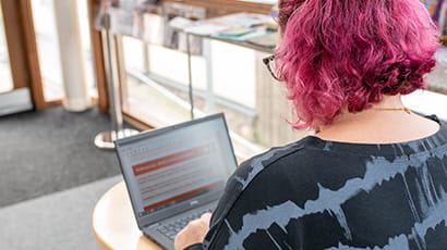 A person with short pink hair working on a laptop
