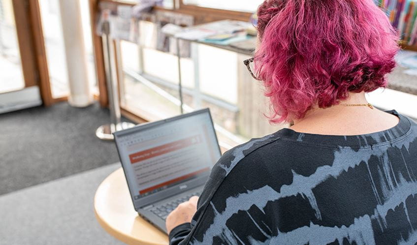 A person with short pink hair working on a laptop