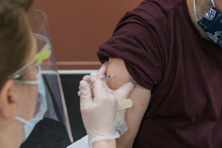 Close-up of person giving injection into patient's arm, both wearing face masks.
