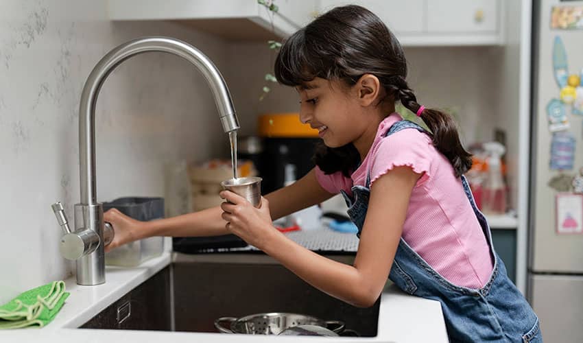 A girl smiling as she fills a cup up with water at a kitchen tap