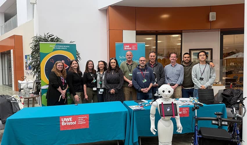 UWE Bristol staff and partners stand behind an information table alongside a humanoid robot at a technology showcase event.