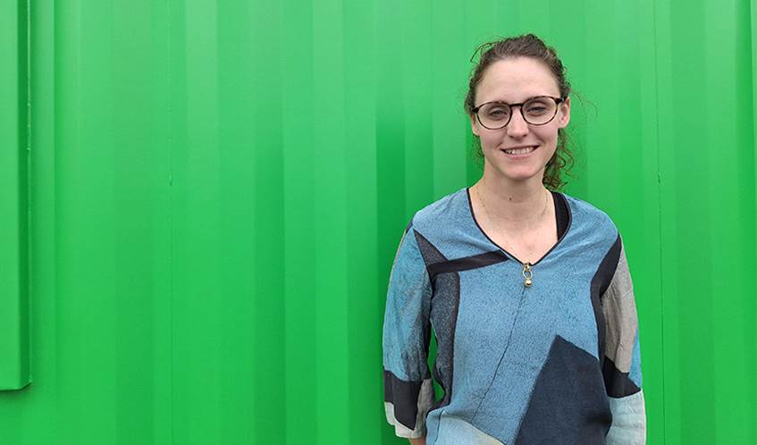 A woman stands in front of a green background.