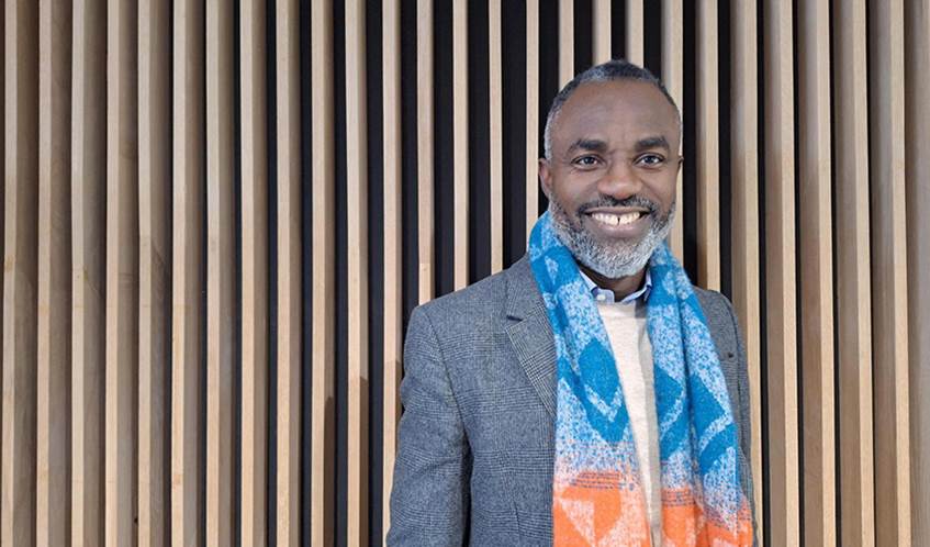 A man smiling looking down the lens of the camera against a wood panel background