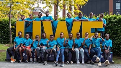 A group of children sit outside on a giant UWE logo, smiling at the camera 