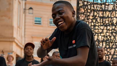 A boy singing and dancing looks at the camera while busking