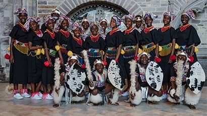A group of school children from South Africa dressed in traditional Zulu attire stand together as a choir