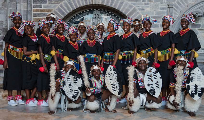 A group of school children from South Africa dressed in traditional Zulu attire stand together as a choir
