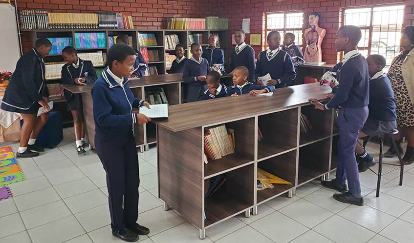 A group of South African school children wearing blue school uniform look at books in a new classroom