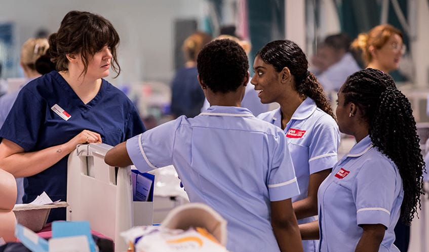 A group of student nurses in a hospital ward setting in conversation with each other.
