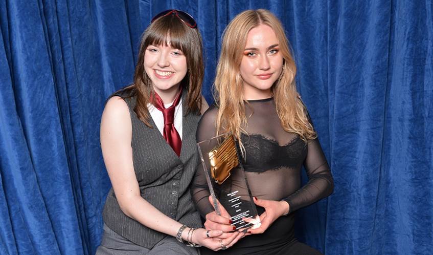 Two winning students smile at the camera whilst holding their award