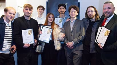 A group of eight students smile at the camera, while holding awards and certificates.
