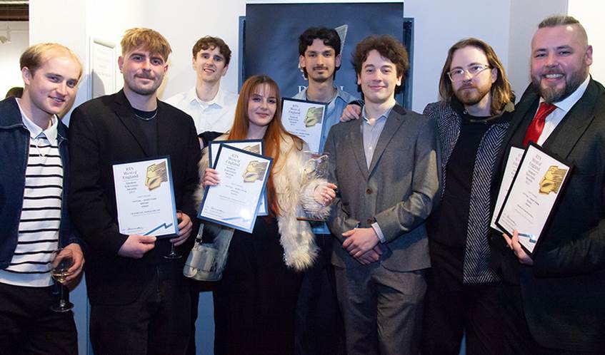 A group of eight students smile at the camera, while holding awards and certificates.