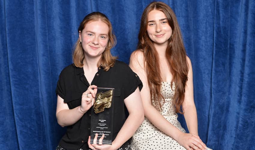 Two people posing with an award trophy in front of a blue curtain backdrop.