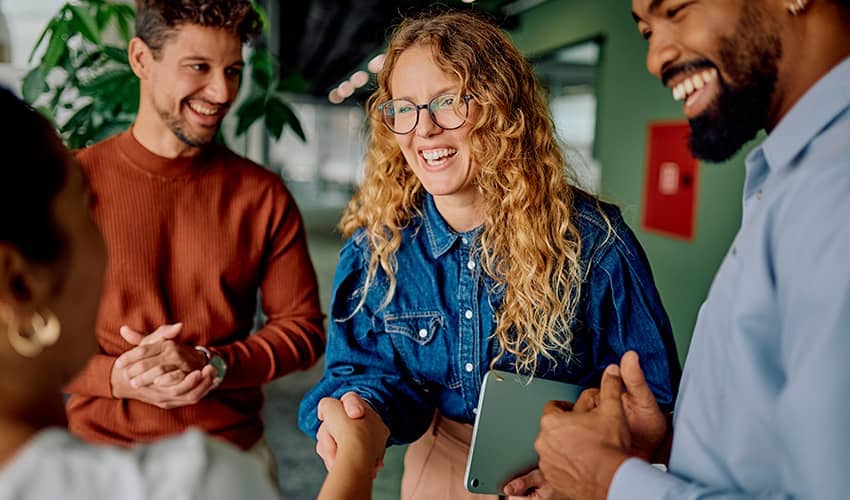 People standing together in conversation, with one person shaking hands in an office setting.