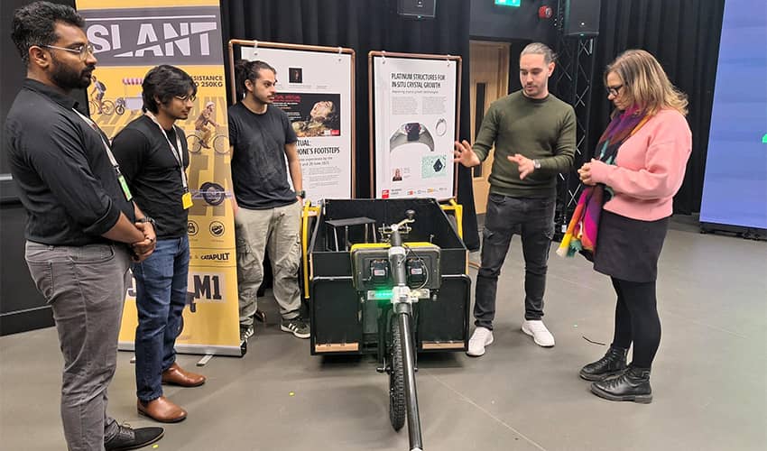 A group of people gathered around a trailer with a large wheel on the front in a studio space. 