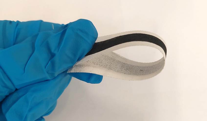 A strip of e-textile is held in a blue-gloved hand.